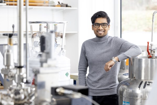 Abhisek Kole stands in the Unisoku scanning tunneling microscope lab. He is leaning against a liquid helium dewar and smiles into the camera.